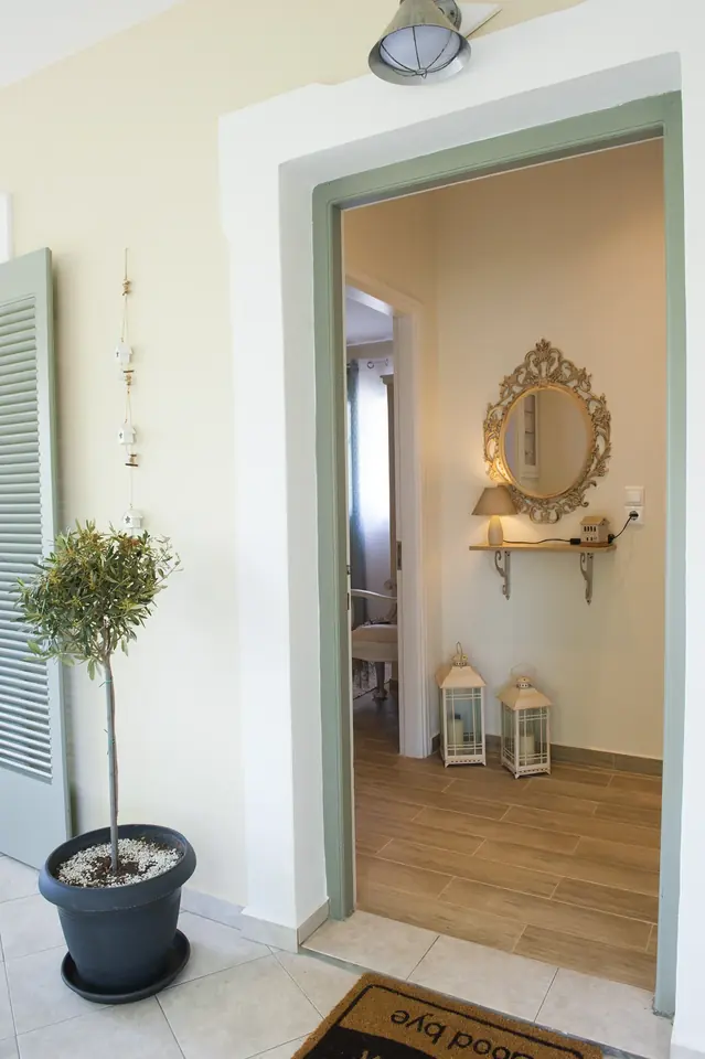 The front door open onto the hallway, beside a potted olive tree